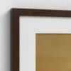 Close-up corner detail of dark brown wooden picture frame with crisp white mat surrounding botanical artwork. The clean corner junction shows the precision craftsmanship where frame meets mat, highlighting the elegant contrast between the rich brown wood frame, bright white matting, and warm tan background of the floral print. Professional framing detail perfect for enhancing botanical wall art in home décor.
