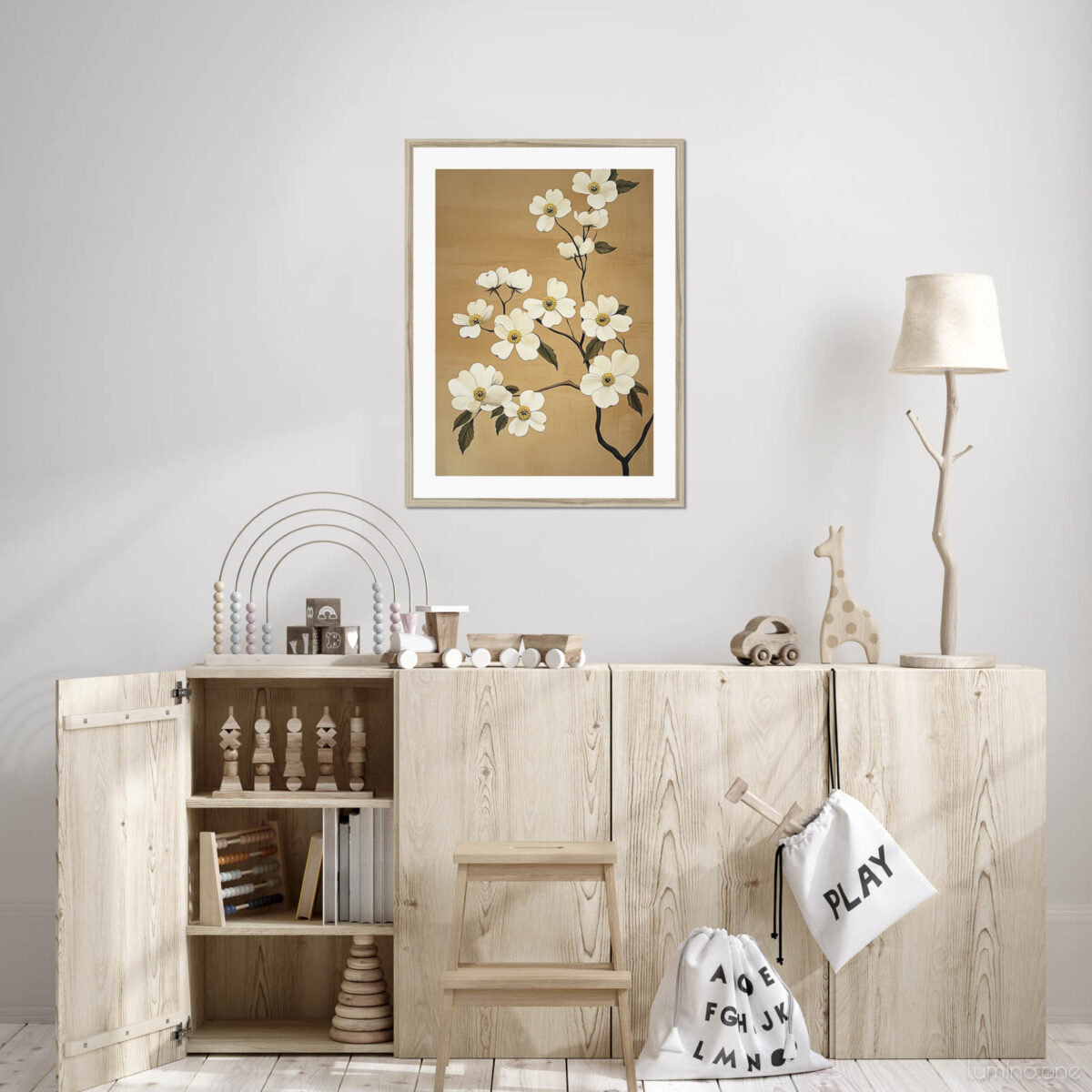 Botanical white flower print in light wood frame hanging above natural wood storage cabinets in Scandinavian-style children's playroom. Elegant floral artwork with tan background complements minimalist nursery featuring wooden toys, rainbow decor, giraffe figurine, branch-shaped lamp, and canvas storage bags. Modern yet warm aesthetic perfect for sustainable nursery or playroom design.