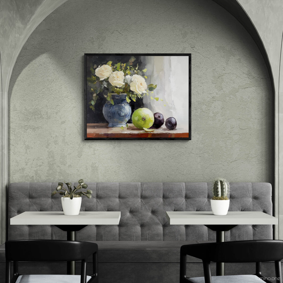 Framed still life oil painting print featuring white roses in a blue ceramic vase with fresh green apple and dark plums on wooden table, displayed in modern cafe or restaurant with arched alcove, gray banquette seating, and white bistro tables