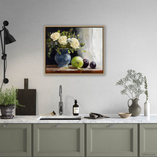 Framed still life oil painting print featuring white roses in a blue ceramic vase with fresh green apple and dark plums on wooden table, displayed above modern kitchen counter with sage green cabinets, marble countertop, and natural wood frame