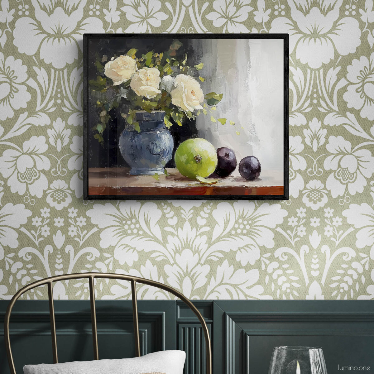 Framed still life oil painting print featuring white roses in a blue ceramic vase with fresh green apple and dark plums on wooden table, displayed in traditional dining room with sage green floral wallpaper, dark wood wainscoting, and brass chair with round table