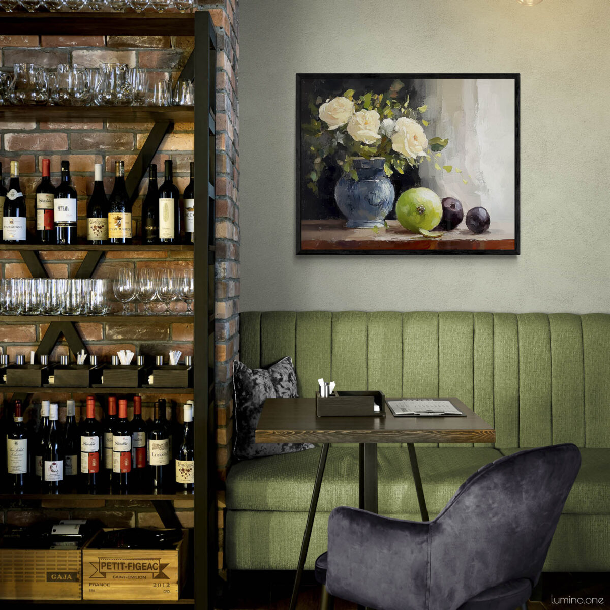 Framed still life oil painting print featuring white roses in a blue ceramic vase with fresh green apple and dark plums on wooden table, displayed in wine bar or restaurant with exposed brick wine storage shelves, green banquette seating, and purple velvet chairs