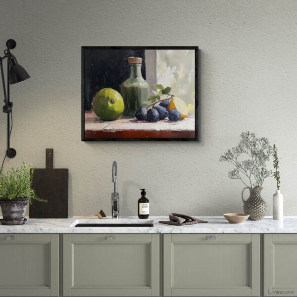 Framed still life oil painting print featuring green apple, dark plums, and green glass bottle with cork arranged on white cloth, displayed above modern kitchen counter with sage green cabinets and marble countertop