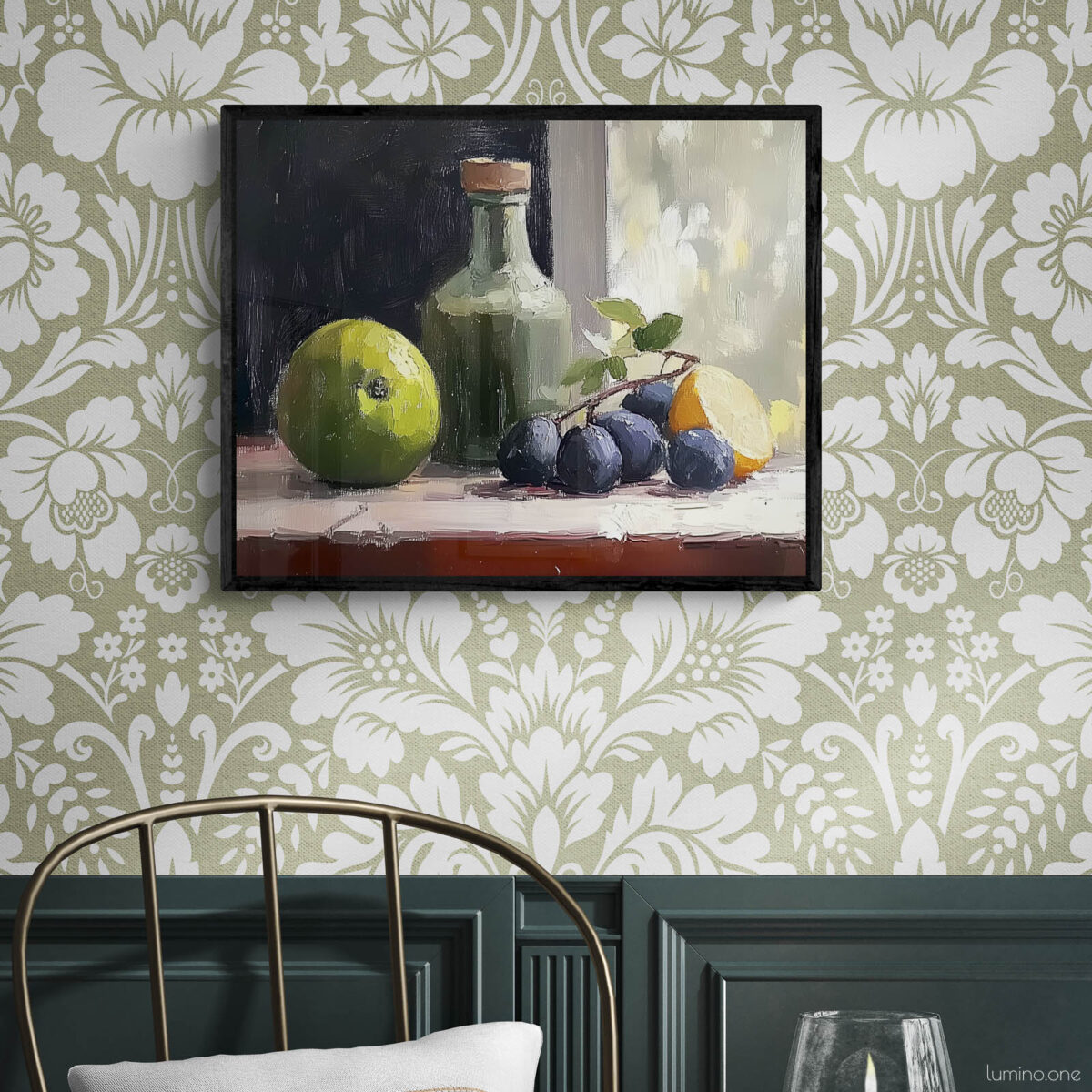 Framed still life oil painting print featuring green apple, dark plums, and green glass bottle with cork arranged on white cloth, displayed in traditional dining room with sage green floral wallpaper, dark wood wainscoting, and brass chair with round table