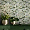 White water lily peel and stick wallpaper styled above dark green painted wood wall paneling with brass gold planters holding fern and pilea plants creating an elegant botanical accent wall