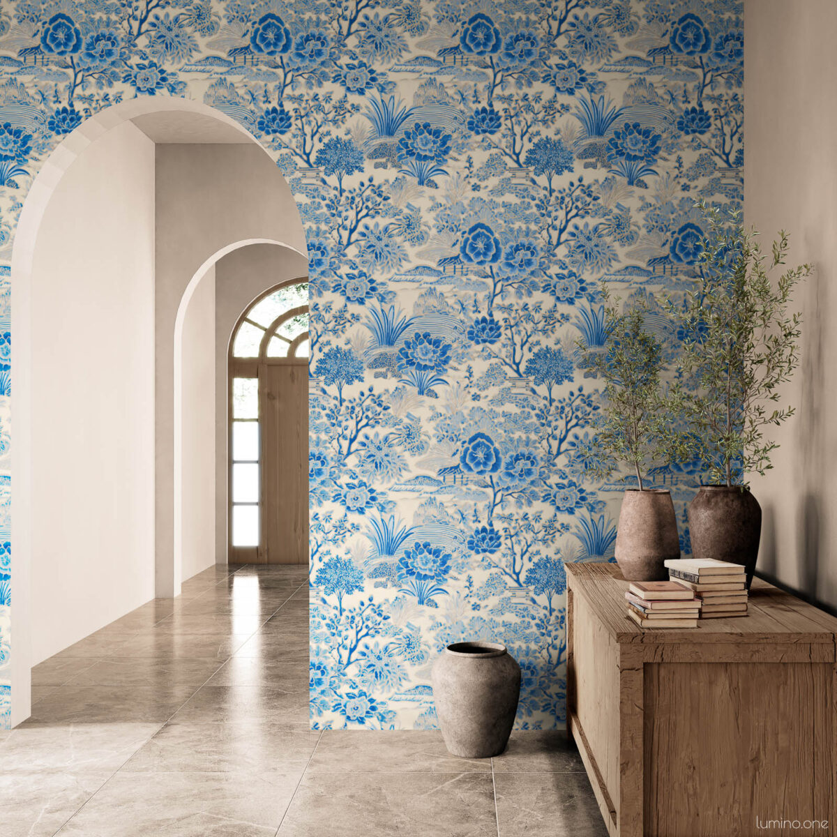 Blue and white toile peel and stick wallpaper on an entryway accent wall in a Mediterranean-style home, featuring a vintage botanical garden pattern with flowers and trees. Styled with a rustic reclaimed wood console, stacked vintage books, terracotta vases with olive branches, and marble tile floors framed by a white arched doorway.