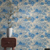 Blue and white toile peel and stick wallpaper on a full wall behind a mid-century modern walnut nightstand, featuring a vintage botanical garden pattern with large peony flowers and trees. Styled with a tall white textured vase holding dramatic white cherry blossom branches, showcasing the wallpaper's scale and detail in a bedroom setting.