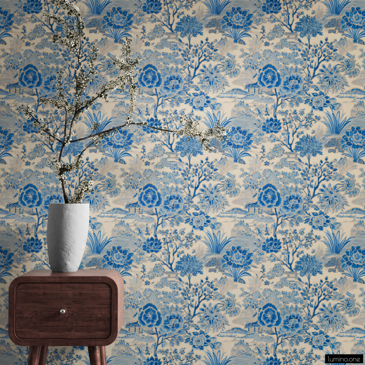 Blue and white toile peel and stick wallpaper on a full wall behind a mid-century modern walnut nightstand, featuring a vintage botanical garden pattern with large peony flowers and trees. Styled with a tall white textured vase holding dramatic white cherry blossom branches, showcasing the wallpaper's scale and detail in a bedroom setting.
