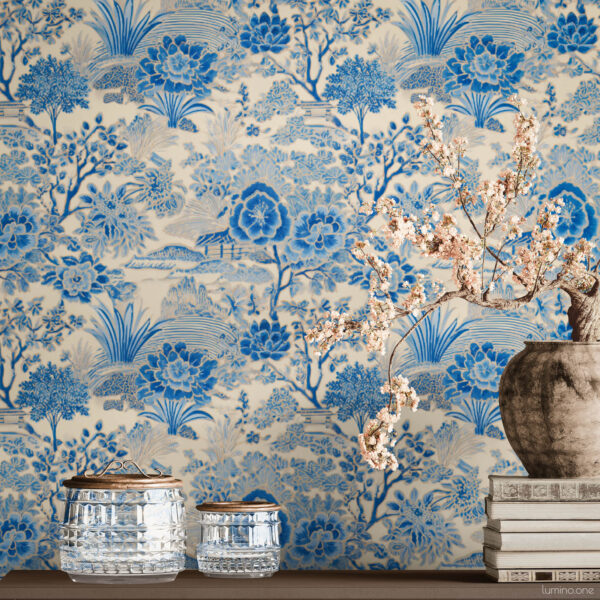 Blue and white toile peel and stick wallpaper on a full wall behind a taupe modern sideboard, featuring a vintage botanical garden pattern with large peony flowers and trees. Styled with a rustic stoneware vase holding cherry blossom branches, stacked vintage books, and crystal glass jars with brass lids.