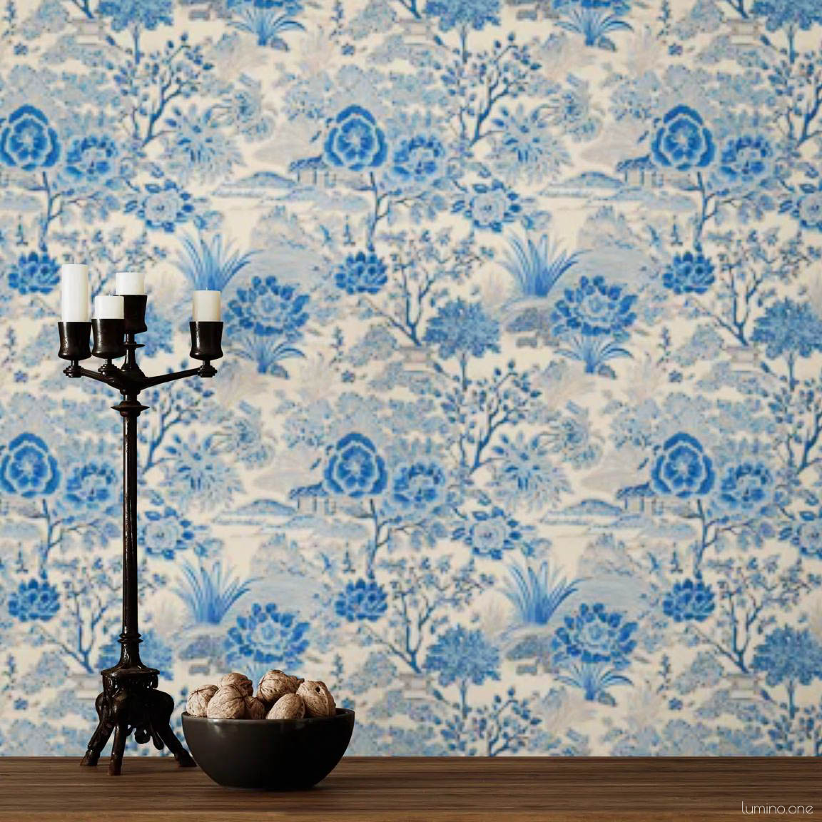 Blue and white toile peel and stick wallpaper covering a full wall, featuring a repeating vintage botanical garden pattern with flowers and trees. Styled with a dark iron candelabra, rustic white vase with red berry branches, and a wood console - living room or dining room accent wall decor.