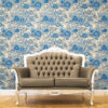 Blue and white toile peel and stick wallpaper covering a full wall behind an ornate French-style tufted leather loveseat with silver carved wood frame, featuring a vintage botanical garden pattern with large peony flowers and trees. Styled on a warm honey herringbone wood floor, showcasing a classic French country living room aesthetic.