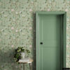 Sage green chinoiserie removable wallpaper with hand-painted birds, pink peonies, and botanical branches in entryway with matching sage green door, round gold side table, pothos plant, and jute rug