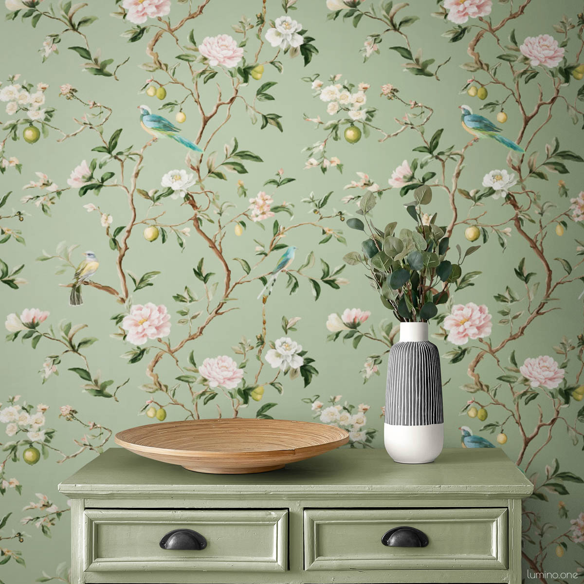 Sage green chinoiserie vintage wallpaper with hand-painted birds, pink peonies, and lemon branches styled with matching sage green dresser with black cup pulls, wooden bowl, and striped ceramic vase with eucalyptus