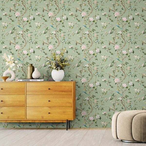 Sage green chinoiserie peel and stick wallpaper with hand-painted birds, pink peonies, and lemon branches in modern living room with beige curved chair, wooden credenza, and white ceramic vases