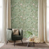 Sage green chinoiserie botanical wallpaper feature wall with hand-painted birds, pink peonies, and lemon branches in bright room with green velvet chair, gold pillow, beige curtains, and natural wood coffee table
