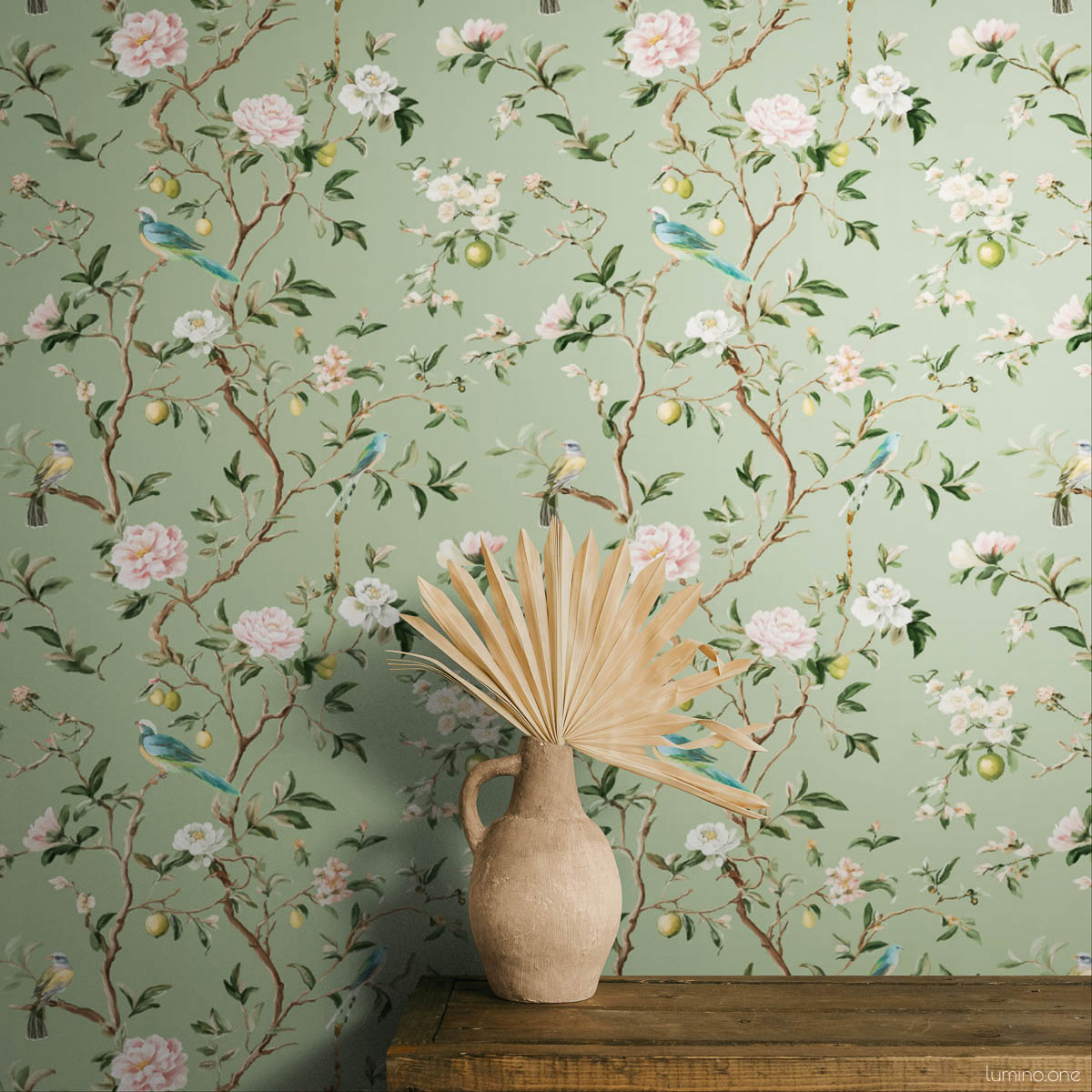 Sage green chinoiserie peel and stick wallpaper featuring hand-painted birds, pink peonies, white blossoms, and lemon branches on botanical background, styled in bedroom with dried palm leaf decor