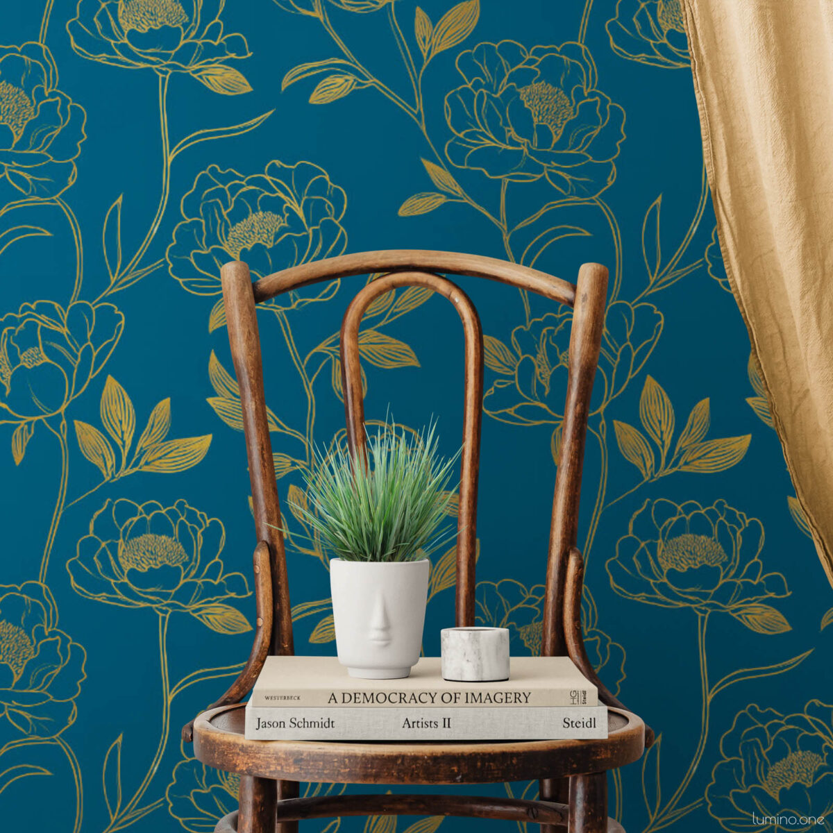 Dark teal and gold peony removable wallpaper styled as a cozy reading vignette with a vintage bentwood chair holding stacked art books, a face planter with grass, and a flowing gold curtain